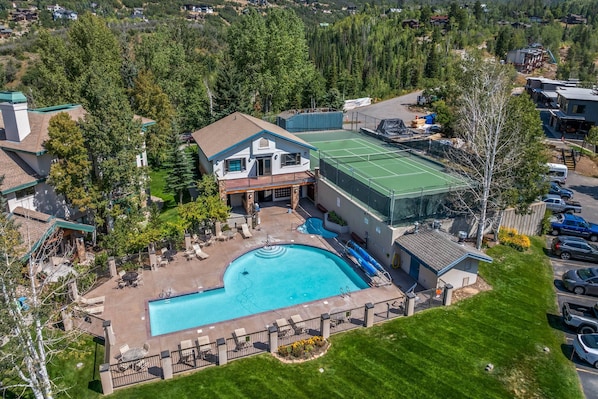 A residential area with a swimming pool, a tennis court, and a large house with a green roof.