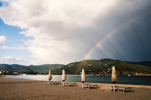 A beach with umbrellas and a mountain backdrop.