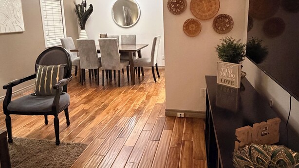 Un comedor con piso de madera, un espejo redondo y una mesa con sillas.