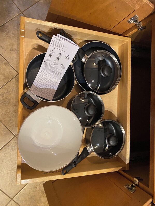 Un cajón de cocina con distintos utensilios de cocina, incluyendo una sartén, una olla y una olla grande.