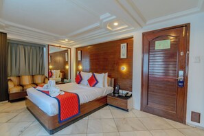 A hotel room with a large bed, a wooden headboard, a nightstand, a mirror, a door with a sign, and a seating area with a sofa. -  Hotel KK By Spree Rajkot (Rajkot)