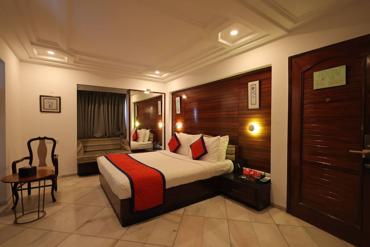 A hotel room with a large bed, a chair, a nightstand, and a wooden door.
