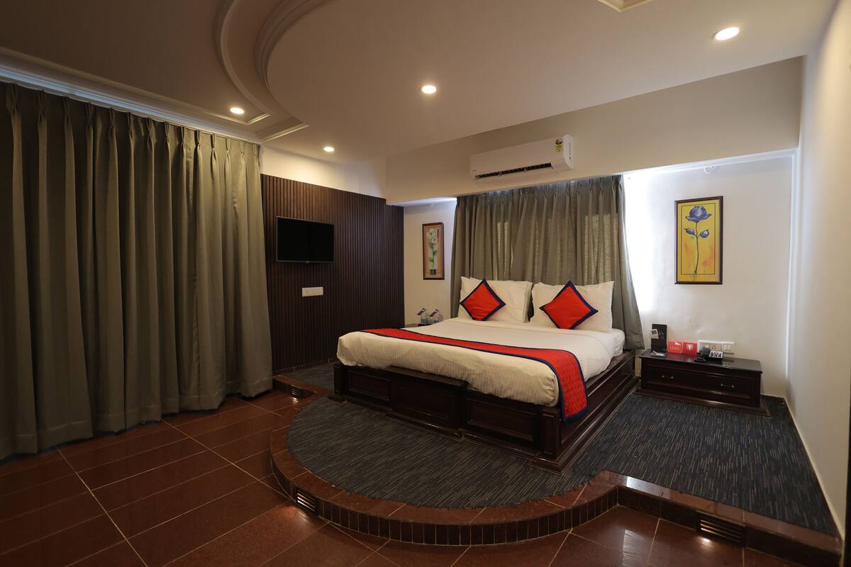 A hotel room with a large bed, a flat-screen TV, a small table with a lamp, and a painting on the wall.