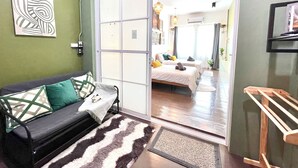 Een moderne woonkamer met een bank, een vloerkleed met patroon en een schuifdeur naar een slaapkamer met een bed en nachtkastje.