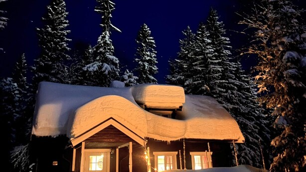 A snow-covered cabin with a sloped roof and a chimney, surrounded by tall evergreen trees. - 8 Person Holiday Home in Salen (Salen)