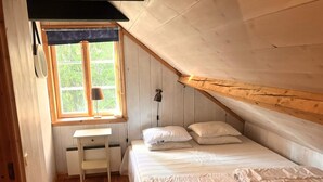 A small, cozy room with a sloped ceiling, a single bed with pillows, a desk with a lamp, and a window with a view of greenery. - 8 Person Holiday Home in Salen (Salen)