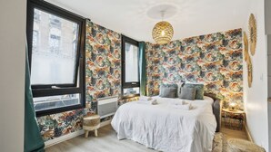 A modern bedroom with a large bed, floral wallpaper, a hanging light fixture, and a view of the city through large windows. - TheBlueStay 144 - Cosy cocoon in Asnières (Paris)