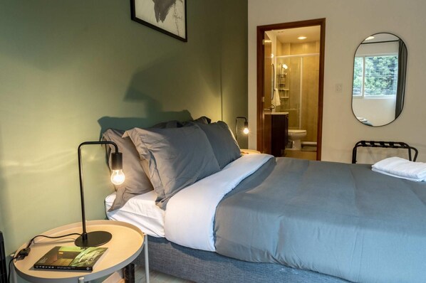 A neatly made bed with a grey and white duvet, a bedside lamp, and a book on a small table beside the bed.