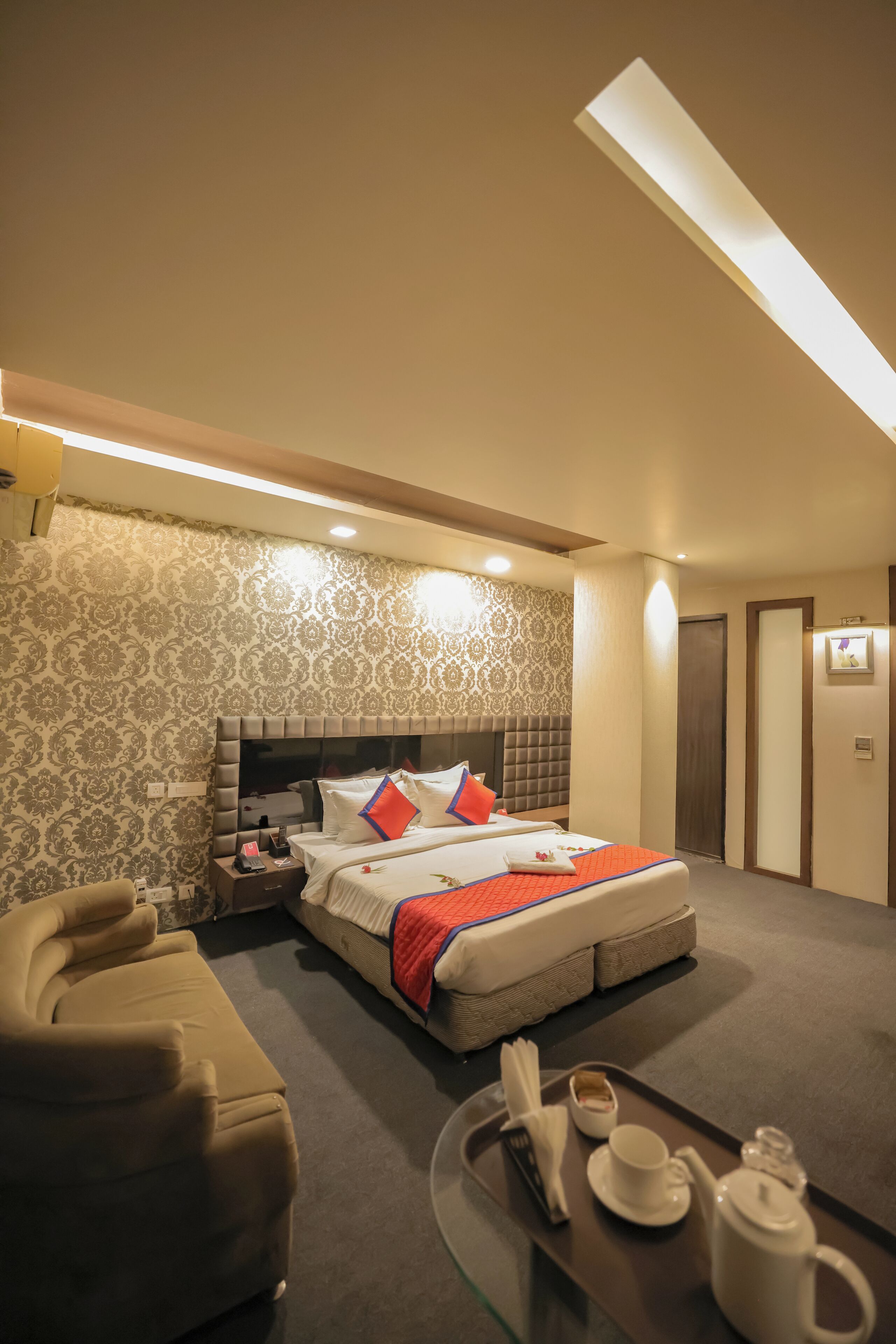 A hotel room with a large bed, a sofa, a tray with tea and a cup, and a patterned wall.