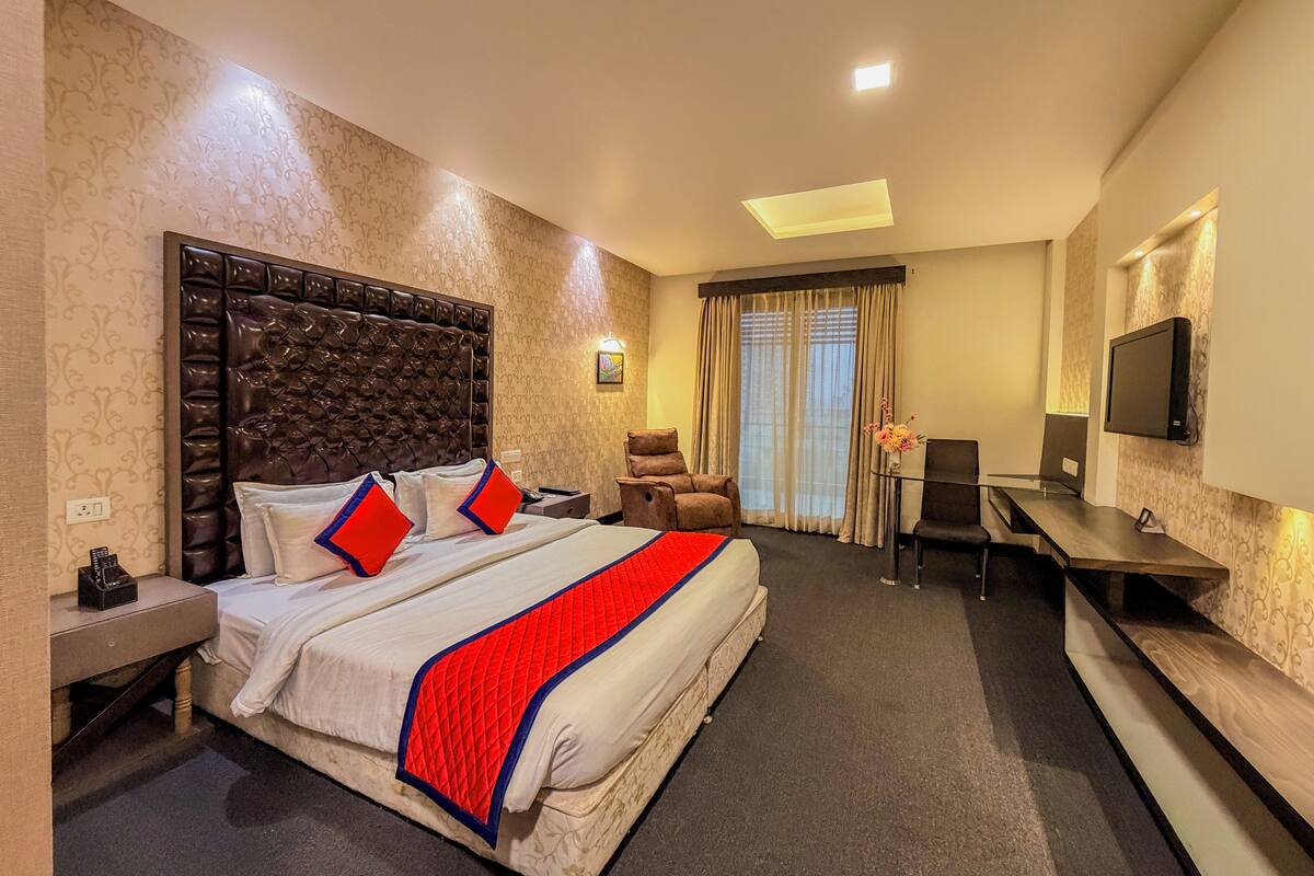 A hotel room with a large bed, a desk, a chair, a TV, and a window with curtains.