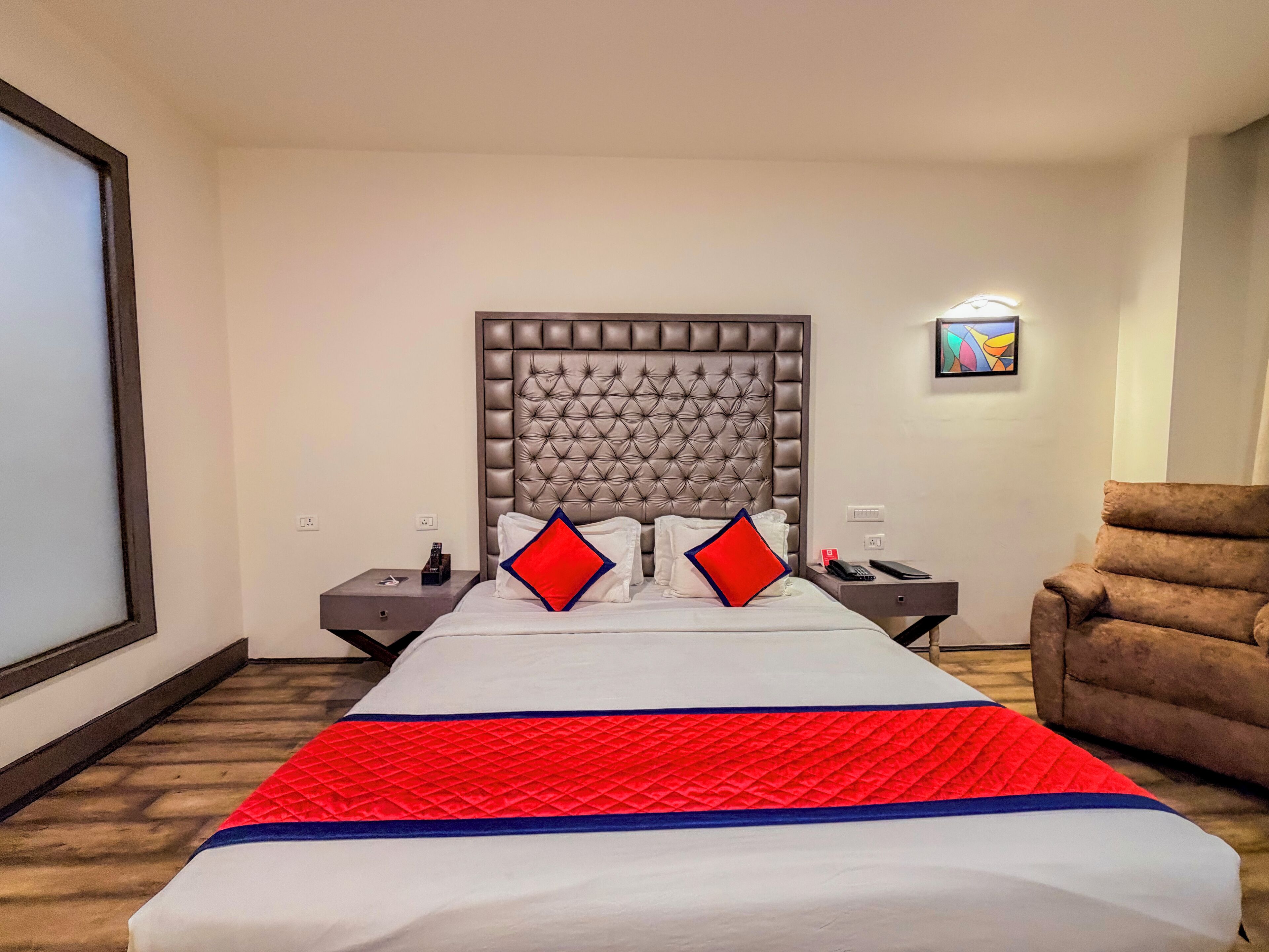 A hotel room with a large bed, a headboard, two bedside tables, a chair, and a wall-mounted artwork.
