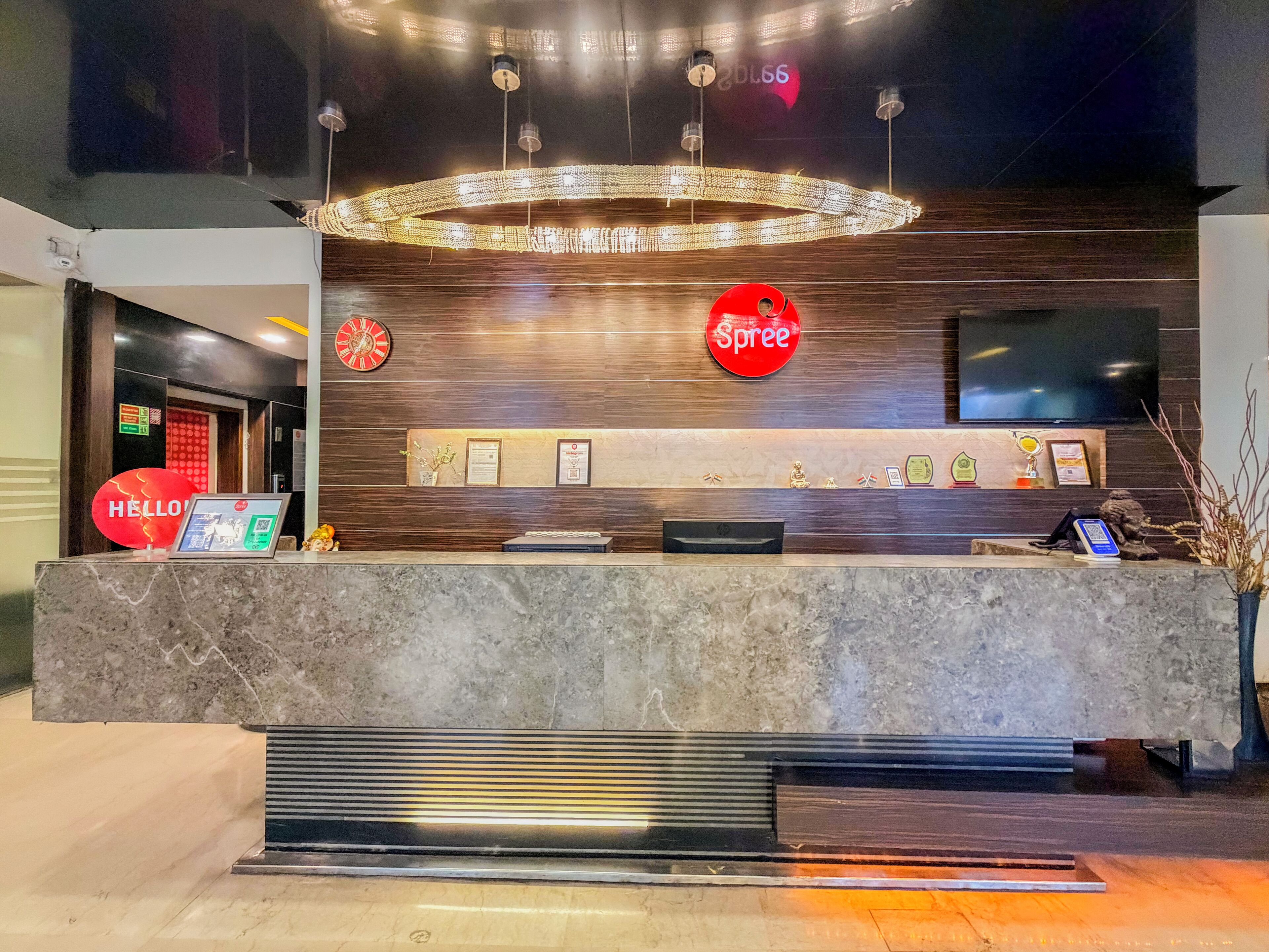 A hotel reception area with a marble counter, a clock, a Spree sign, framed certificates, and a television.