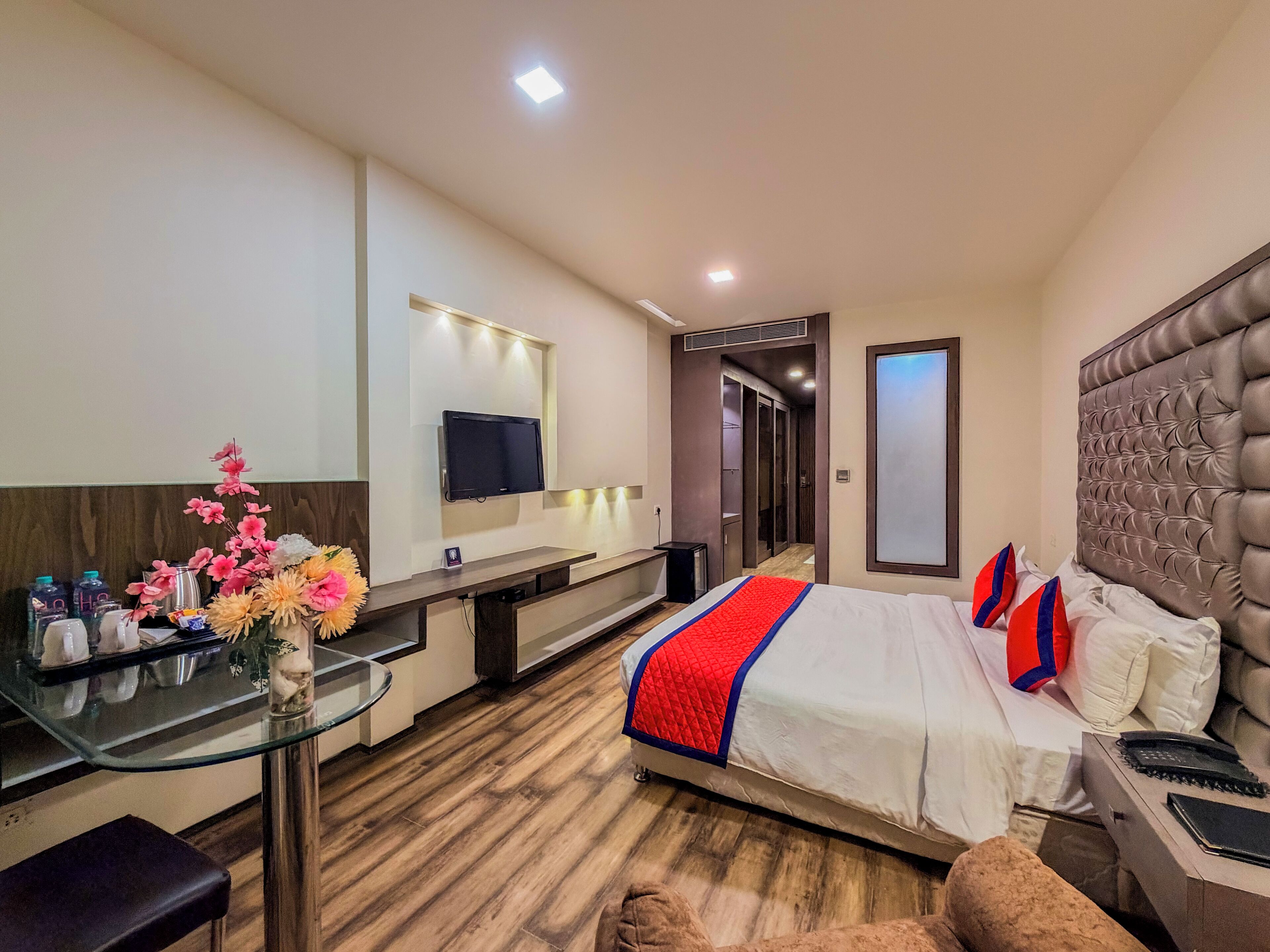 A hotel room with a bed, bedside table, TV, and a desk with a chair.