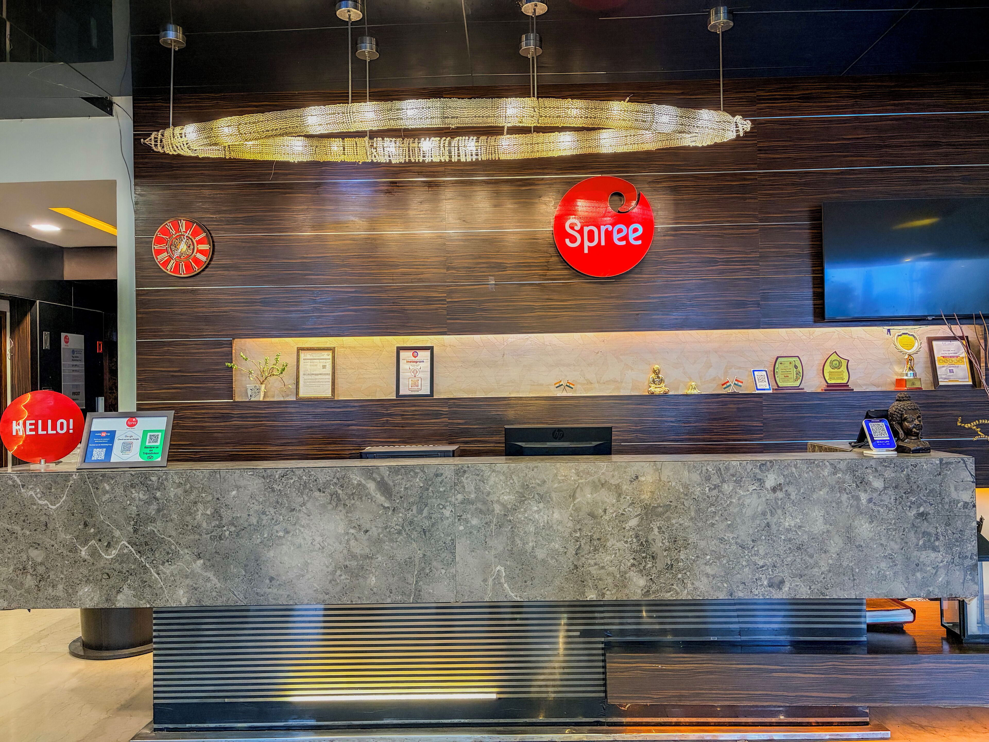 Ein Hotelrezeptionstresen mit einem 'Spree'-Schild, einer Uhr, gerahmten Zertifikaten und einer Buddha-Statue.