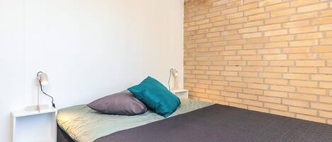 Ein Schlafzimmer mit einem Bett, einem Nachttisch, einer Lampe und einer Ziegelwand.