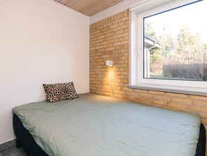 A bedroom with a single bed, a window, and a brick wall.