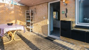 Une terrasse ensoleillée avec une table et des chaises, un mur en briques, un plafond en bois et une fenêtre.