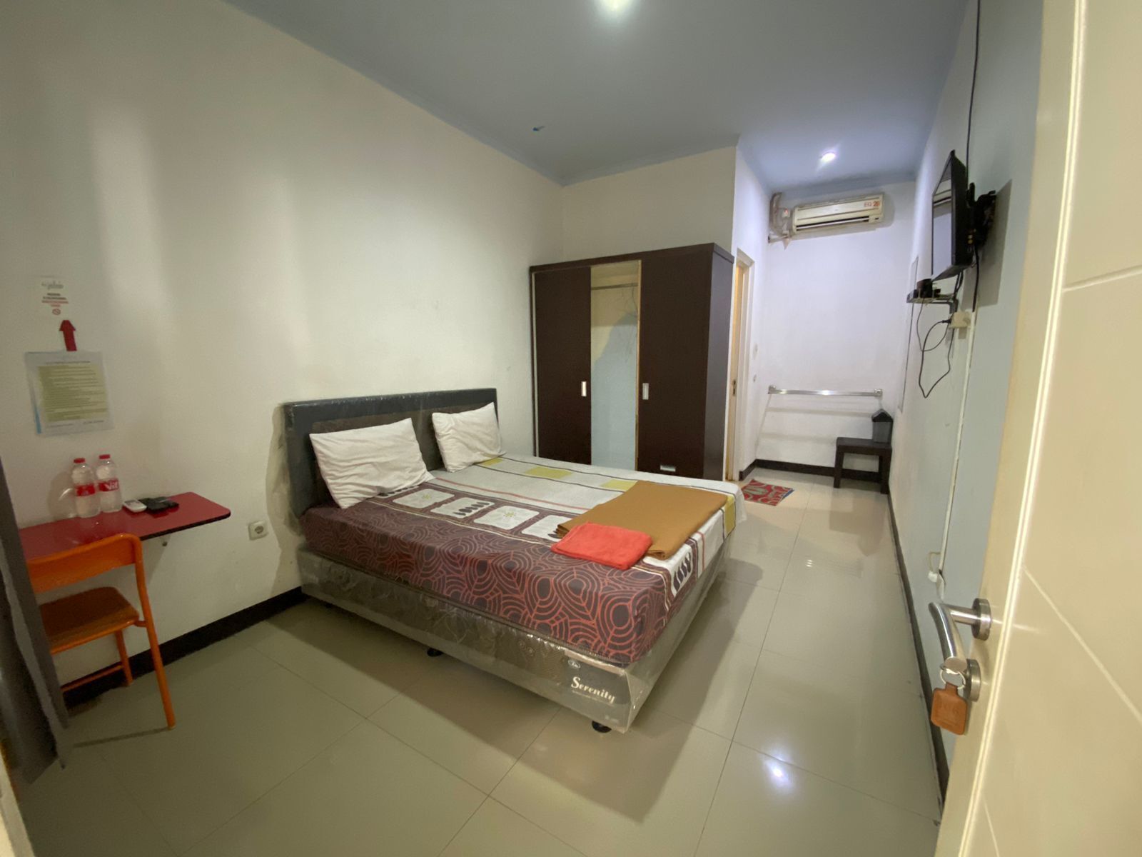A hotel room with a bed, a desk, a chair, an air conditioning unit, and a wardrobe.