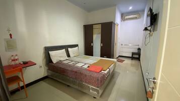 A hotel room with a bed, a desk, a chair, an air conditioning unit, and a wardrobe.