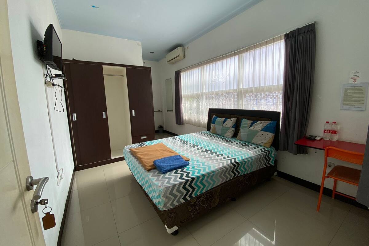 A bedroom with a bed, a desk, a chair, a wardrobe, and a window with curtains.