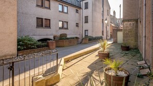 Une rue étroite, bordée de bâtiments des deux côtés, avec une clôture en métal et des plantes en pot.