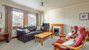Un salon comprenant un canapé, un fauteuil rouge, une table basse en bois, un téléviseur et une cheminée.