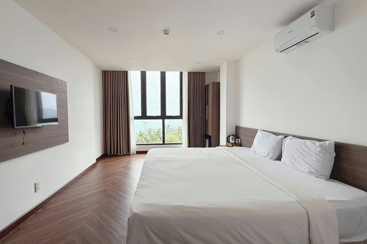 Ein modernes Hotelzimmer mit einem großen Bett, einem flachbildfernseher an der Wand und einem großen Fenster mit Blick ins Freie.
