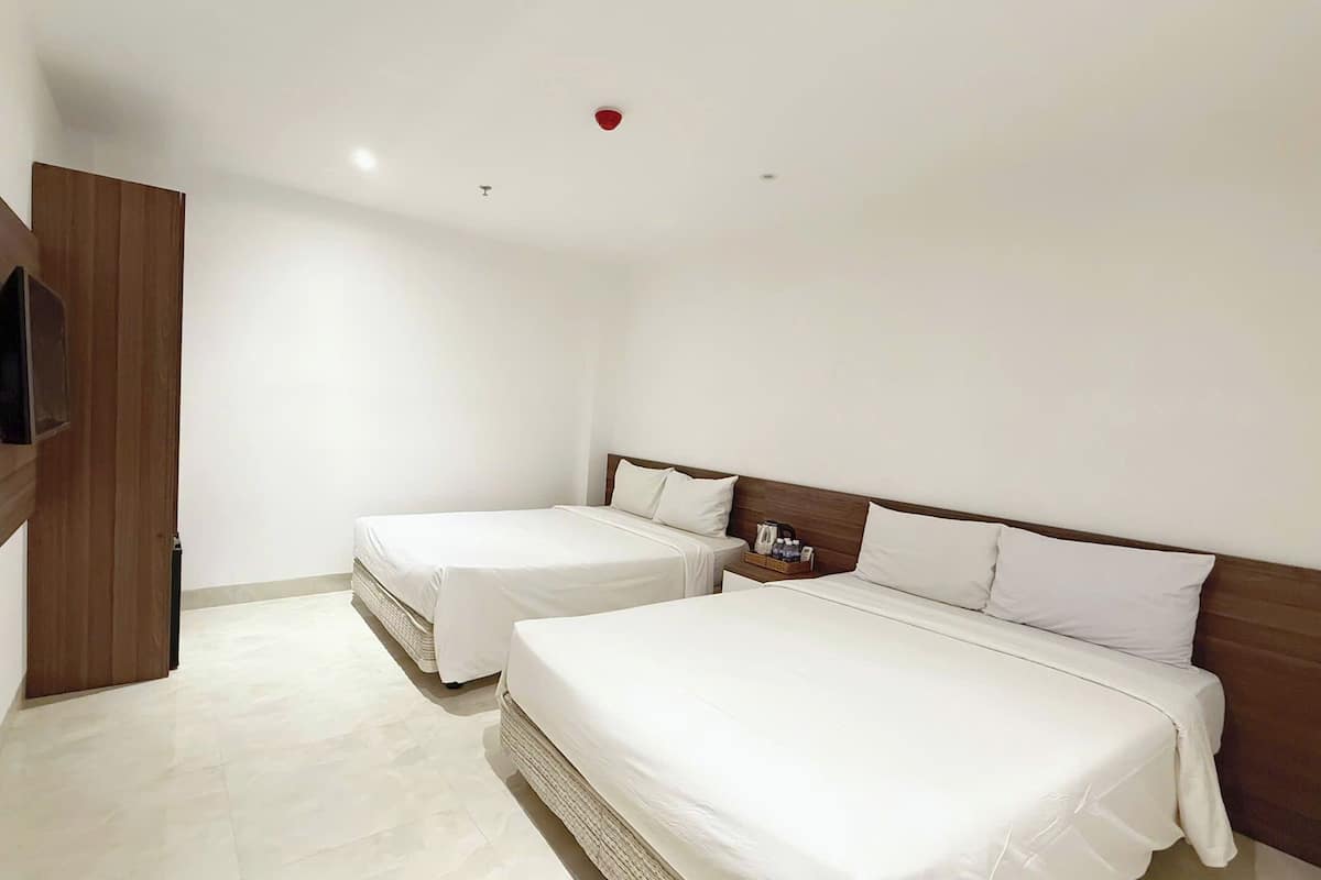 Ein Hotelzimmer mit zwei Betten, einem an der Wand montierten Fernseher und einem kleinen Nachttisch mit einem Korb.