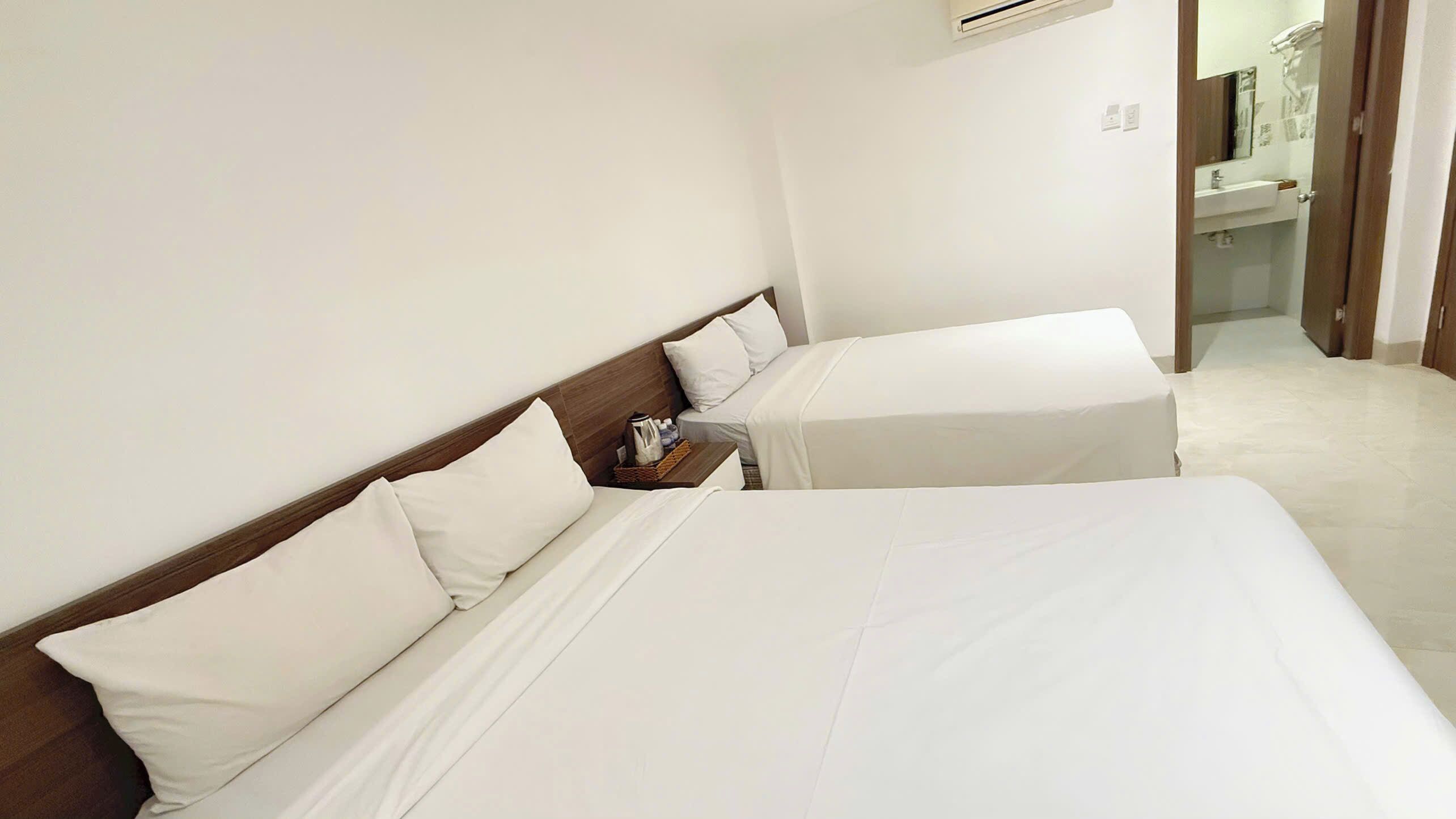 A hotel room with two beds, a nightstand, and a bathroom visible through an open door.