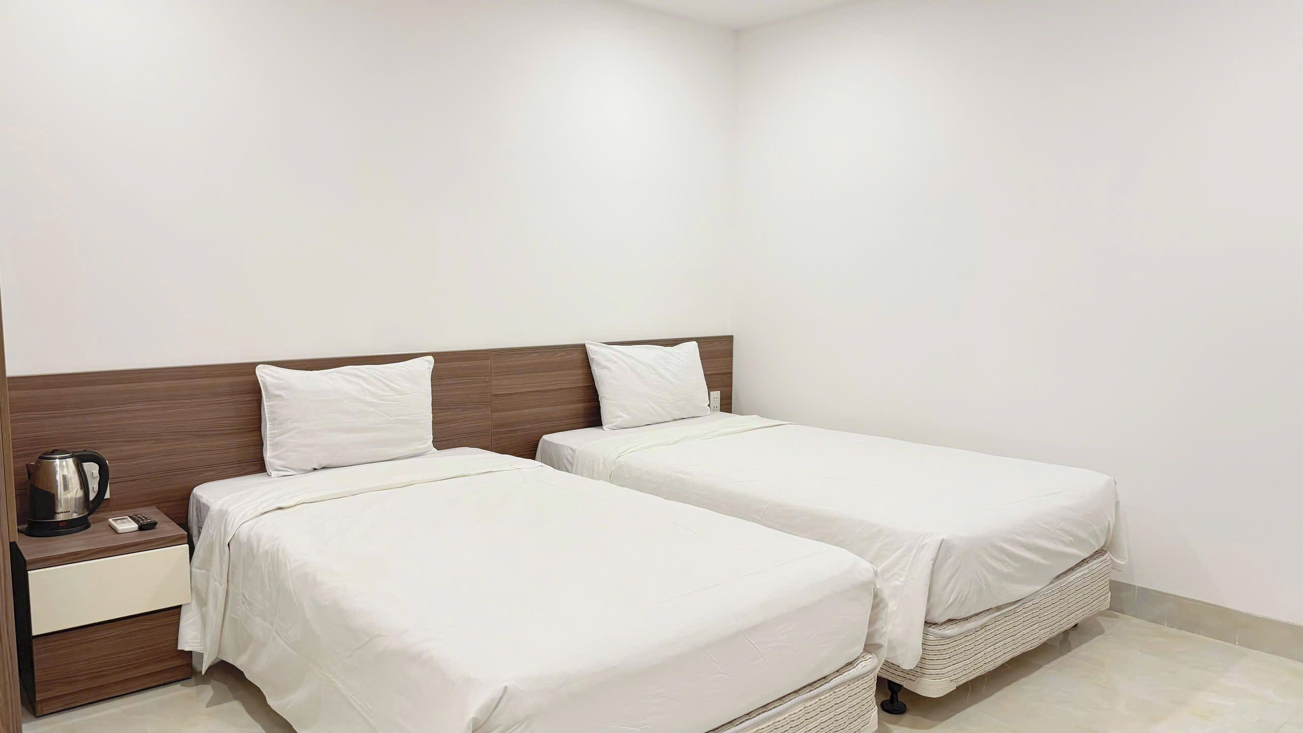 Habitació d'hotel amb dos llits individuals, un capçal de llit de fusta, una taula de nit amb una paperera i un calaix petit.