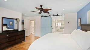 A bedroom with a bed, a dresser, a ceiling fan, and a door leading to another room. - DU Haven- Hot Tub, Outdoor TV Lounge &3 Full Baths (Denver)