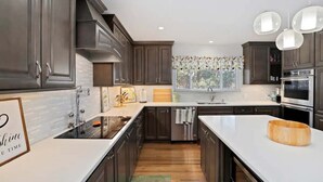 A modern kitchen with dark wood cabinets, white countertops, stainless steel appliances, and a large island. - DU Haven- Hot Tub, Outdoor TV Lounge &3 Full Baths (Denver)