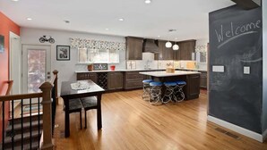 A modern kitchen with wooden cabinets, a bar area, and a chalkboard wall with 'Welcome' written on it. - DU Haven- Hot Tub, Outdoor TV Lounge &3 Full Baths (Denver)