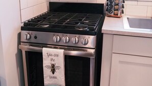 Une cuisine équipée d’une cuisinière, d’un four et d’une hotte aspirante en acier inoxydable. On y trouve une fenêtre donnant sur l’extérieur, un évier et un porte-épices.