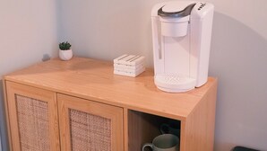 Un meuble en bois contenant une machine à café, une petite plante en pot et un miroir accroché au mur.