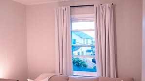 Un canapé beige avec des coussins blancs, un plancher en bois, une fenêtre avec des rideaux et un luminaire au plafond.