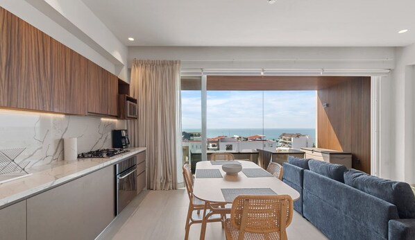 A modern kitchen with a dining area, a sofa, and a view of the sea. - Maralma 903: Panoramic Views and Rooftop Pool (Bucerías)