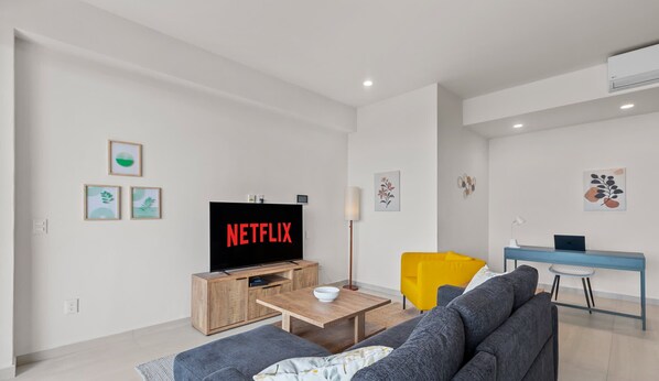 Un salon moderne avec un téléviseur à écran plat, un canapé, une table basse et un bureau avec un ordinateur portable.