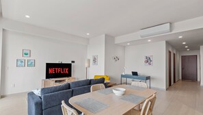A modern living room with a sofa, a dining table, and a TV displaying 'NETFLIX'. - Maralma 903: Panoramic Views and Rooftop Pool (Bucerías)