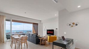 A modern living room with a large TV screen, a dining area, and a view of the sea. - Maralma 903: Panoramic Views and Rooftop Pool (Bucerías)