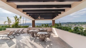 A terrace with a table and chairs, a ceiling fan, and a view of a cityscape and mountains. - Maralma 903: Panoramic Views and Rooftop Pool (Bucerías)