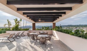 Una terraza con mesa y sillas, un ventilador de techo y vistas a un paisaje urbano y montañas.