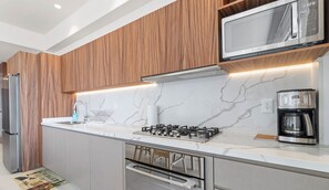 Une cuisine moderne avec des meubles en bois, un réfrigérateur en acier inoxydable, un four à micro-ondes, une cuisinière à gaz et une machine à café.