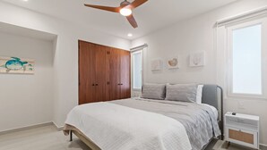A bedroom with a bed, a wardrobe, a ceiling fan, a window, and wall art. - Maralma 903: Panoramic Views and Rooftop Pool (Bucerías)