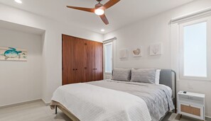 Un dormitorio con cama, armario, ventilador de techo, ventana y decoración en la pared.