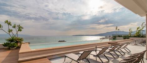 A poolside area with lounge chairs and a view of the sea.