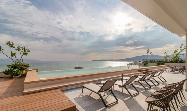 A poolside area with lounge chairs and a view of the sea. - Maralma 903: Panoramic Views and Rooftop Pool (Bucerías)