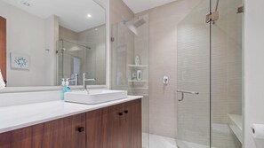 A modern bathroom with a glass shower enclosure, a white sink, and a wooden vanity. - Maralma 903: Panoramic Views and Rooftop Pool (Bucerías)