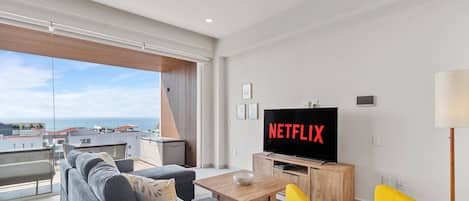Un salon moderne doté d’un grand téléviseur à écran plat, d’un canapé, d’une table basse et offrant une vue sur la mer.