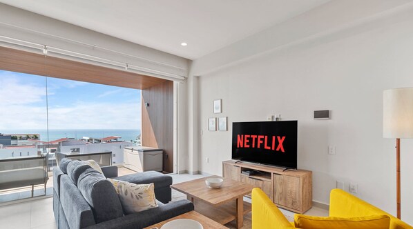 A modern living room with a large flat-screen TV, a sofa, a coffee table, and a view of the sea. - Maralma 903: Panoramic Views and Rooftop Pool (Bucerías)